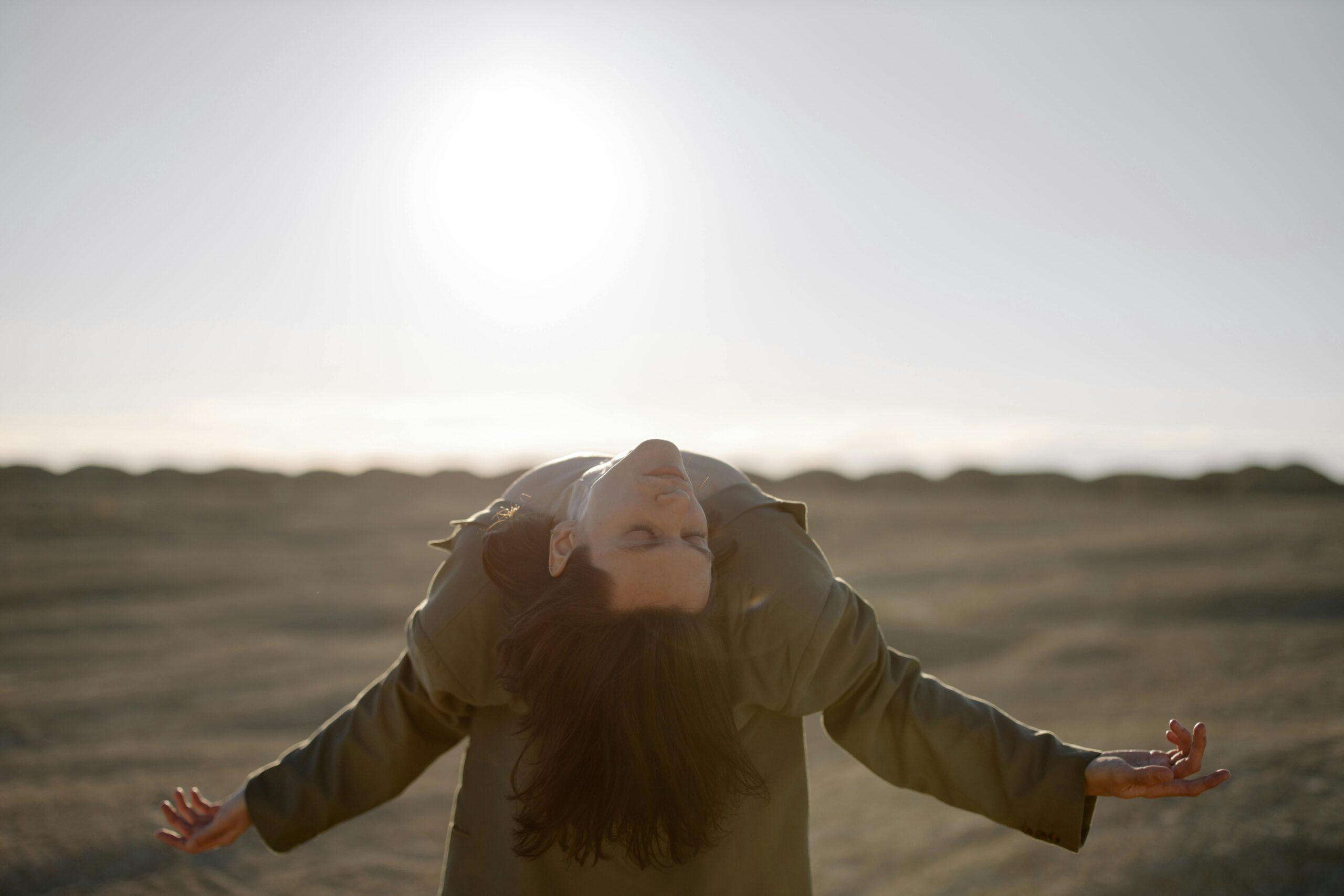 A male dancer posing dramatically under the bright sun in a vast desert landscape.
